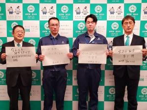 宮古市のバックパネルをバックに石川県能登町災害派遣職員2名の方たちが中央に並び両隣に市長と関係者1名がパネルを持ちながら記念撮影をしている写真
