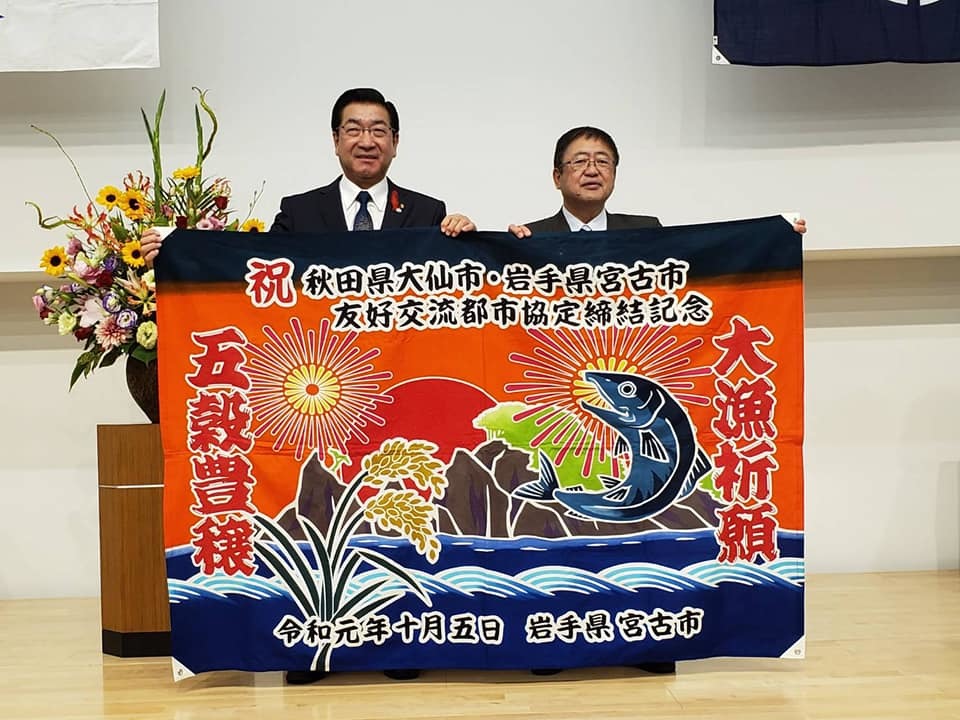 大漁旗を持ち広げる市長と男性の記念写真