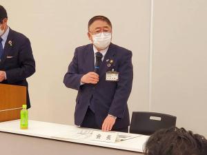 「会長」と書かれた席札が置かれた自席から立ち上がった市長が、右手にマイクを持ち話をしている様子の写真
