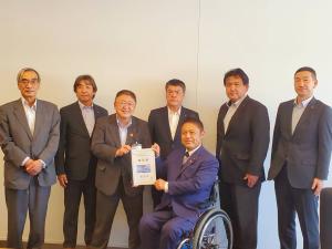 車いすに座った男性と市長が一緒に要望書を持ち、その周りに横並びに立つ男性5名を写した写真