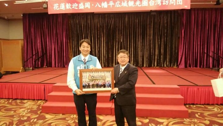 赤色のステージの上に「花蓮歓迎盛岡・八幡平広域観光圏台湾訪問団」と書かれた横断幕が掲げられ、ステージの下で魏嘉賢花蓮市長と市長が額入りの写真を一緒に持っている写真