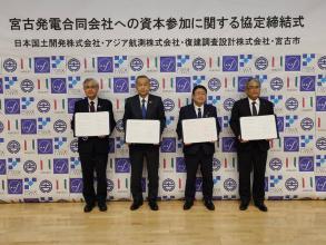 宮古発電合同会社への資本参加に関する協定締結式と書かれた横断幕の下で市長と日本国土開発株式会社、アジア航測株式会社、復建調査設計株式会社の代表方々がサインをした協定書をそれぞれ持って、並んで撮影した写真