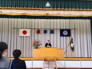 宮古市立第二中学校体育館の舞台の白い幕に「祝卒業」の文字と日の丸と市章が飾られ演台で挨拶をしている市長の写真