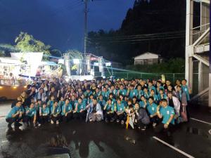 ライトアップされた船山車をバックに、青の羽織を着た市長を中心にして、お揃いの緑色のTシャツを着た参加者の方々が集合して撮影した写真