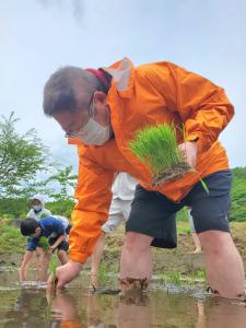 オレンジ色のパーカーを着て田植えをする様子の市長の写真