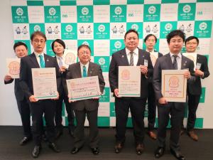 バックパネルの前で、一人ずつボードを持った市長や副市長、6名の関係者が2列に並んでいる写真