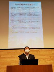 宮古市気候非常事態宣言の内容が映し出されたスクリーンを背景に 市長が演台で説明している写真