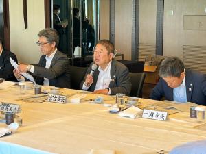 大きなテーブルの上に「宮古市長」と書かれた席札が置かれた席に座った市長が、右手にマイクを持ち話をしている写真