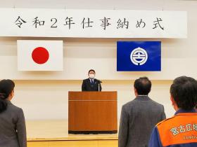 令和2年仕事納め式と書かれた横断幕の下、市長が演台に立ち、参加者へ向けて式辞を述べている写真