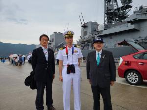 停泊する海上自衛隊護衛艦「まきなみ」の前で、双眼鏡を首にかけた船長を中心に、市長と関係者の男性が並んで写る記念写真