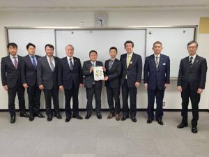 ホワイトボードの前で、石渡史浩三陸国道事務所長と市長が要望書を一緒に持ち、7名の関係者が横一列に並んでいる写真
