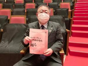 市民文化会館の観客席に座り、両手で「ベートーヴェン『交響曲第9番』を踊る」のパンフレットを持っている市長の写真