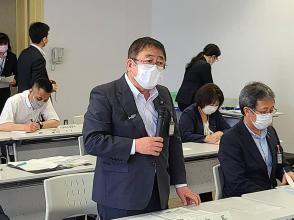 4地区合同会議で資料が置かれたテーブルの前に立った市長が片手でマイクを持ちながら話をしている写真