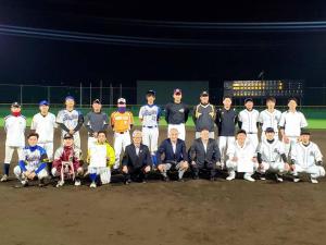 夜の野球場で、前列に関係者の男性やユニフォームを着た選手たちが9名しゃがみ、後列にユニフォームを着た選手たち12名が立って横並びになり写っている写真