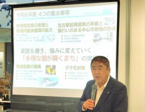 スクリーンに映し出された画像の横で、市長がマイクを持ち、話をしている写真