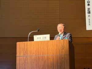 檀上に立つ市長がマイクを右手で持ち挨拶を行っている、インフラマネジメントシンポジウム2023の様子の写真
