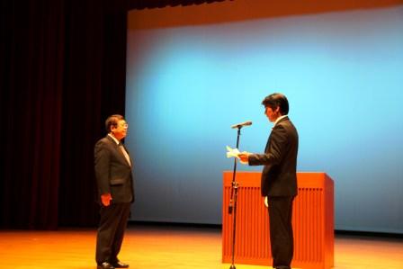 ステージ上で田嶋勝正串本町長が義援金の目録を読み上げているのを、山本市長が聞いている写真