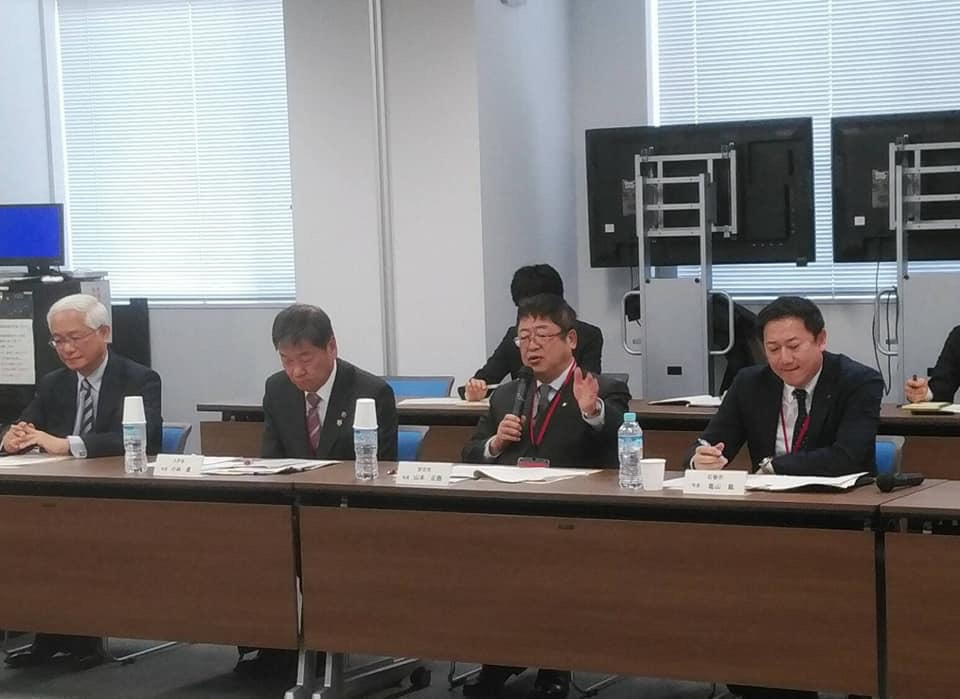 2列に並べた長机の席に参加者が2名ずつ座った震災伝承検討会が行われた会場で、自席に座った市長が右手にマイクを持ち話をしている様子の写真