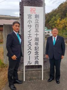 「宮小サイエンススクール創立150周年記念式典」と書かれた立て看板を挟んで市長と関係者の男性が立っている写真