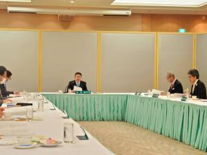 長机がコの字に配置された会議室で、市長、参加者の方々が自席に座り、資料に目を通している写真
