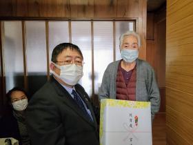 ご自宅で、市長が市からの記念品を持ち、野崎シゲさんとご家族1人と撮影した写真