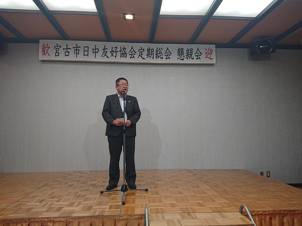 「宮古市日中友好協会定期総会 懇親会」と書かれた横断幕が掲げられた舞台上で、スタンドマイクに向かい話をする市長の写真