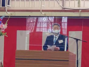自衛官候補生入隊式で紅白の幕をバックにアクリル板が置かれた演台の前で市長が祝辞を述べている写真