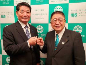 バックパネルの前でグータッチをしている市長と男性の写真