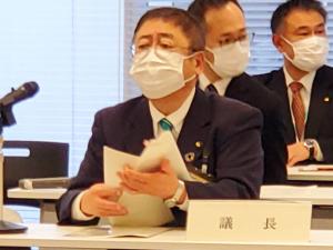 市長が議長と書かれたネームプレートの席に座り、資料を開いている写真
