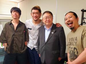 右から口を大きく開けて笑う男性、スーツ姿の市長、市長の肩に手を掛けてほほ笑む男性、両手をポケットに入れた男性が並んでいる記念写真