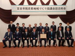 宮古市脱炭素地域づくり協議会設立総会と書かれた横断幕の下で市長が総会に参画いただいた団体の関係者の皆さんと横2列に並んでいる写真