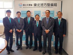 東北地方整備局内のパネルの前で同じ水色のネクタイをした宮古市から市長を含めた5名の関係者と東北地方整備局の担当者のかたと1列に並んで記念撮影をしている写真