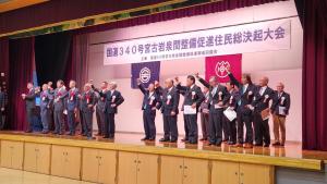 「国道340号宮古岩泉間整備促進住民総決起大会」と書かれた横断幕が吊るされたステージ上に上がった多くの参加者が右手を突き上げている写真