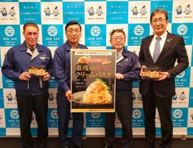 市長と山崎義広組合長が重茂の焼きうにクリームパスタのポスターを持ち、後川良二業務部長と市の職員がクリームパスタの商品を持って、並んで撮影した写真