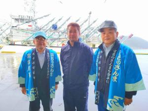 停泊する漁船の前で、青い法被を着た市長と関係者の男性が両側に立ち、中央に紺色のジャージを着た関係者の男性が1名並んで写っている写真
