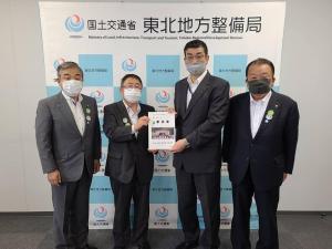 「国土交通省 東北地方整備局」と書かれたバックパネルの前でスーツ姿の男性4名が並び、市長と男性1名が中心で一緒に要望書を持って記念撮影をしている写真