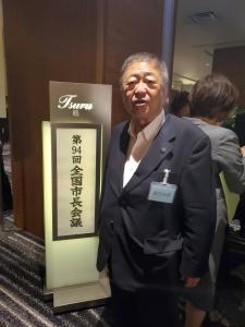 「第94回全国市長会議」と書かれた看板の前で立つ市長の写真