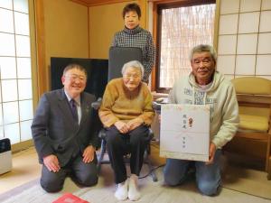 100歳を迎えた馬場ミヨさんを中心に、市長と贈呈品を持ったご家族の男性が両側に並び、後方に女性が立って写る記念写真