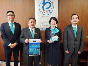写真がプリントされた袋を持ち正面に向ける市長、その右隣に立つ森澤恭子区長、2人の両側に立つ男性の4人を写した写真