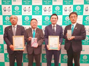 バックパネルの前で目録を持った市長を中心に、額縁を持った2名の男性、LED防犯灯を持った男性1名が横一列に並んでいる写真