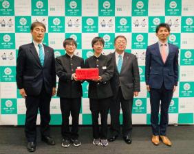 宮古市のバックパネルをバックに崎山中の男子生徒2名が能登半島地震災害義援金の箱を持って市長と関係者の方にはさまれて5人で記念撮影をしている写真