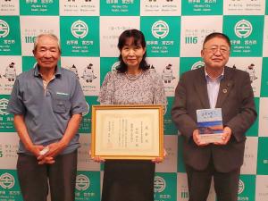 中央に賞状を両手で持った2021年度岩手県芸術選奨を受賞した田老出身の作家・田沢五月さん、左側に高屋敷登さん、右側に市長が立ちバックパネルの前で並んでいる写真