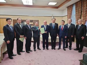 国旗が置かれた室内で、鈴木俊一財務大臣と市長が要望書を一緒に持ち、7名の県内首長の方々と横一列に並んでいる写真