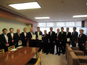 要望書を持つ男性2名と、市長を含む関係者の男性たち11名が横一列に並ぶ記念写真