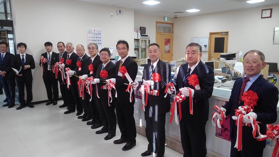 北りあす支店の室内で、市長と8名の関係者が横一列に並びテープカットが行われた直後の開店セレモニーの様子の写真