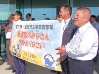 「派遣団のみなさん おかえりなさい」と書かれた横断幕を手に持つ関係者と、拍手で迎える市長の写真