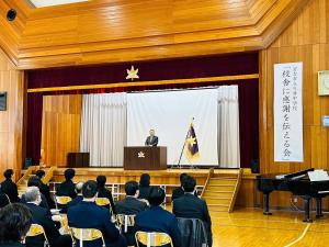 関係者の方々がパイプ椅子に座りながら体育館で行われている「川井中学校校舎に感謝を伝える会」でステージにたち挨拶をしている市長の写真