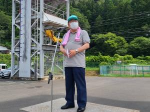 ピンクのタオルを首にかけ、緑色の帽子を被った市長がスタンドマイクの前で話をしている様子の写真
