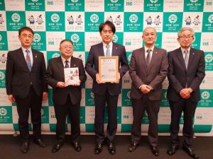 宮古市のバックパネルの前で、額入りの証を持った株式会社トライスの男性担当者と2名の関係者、のし袋を持った市長と副市長が横一列に並んでいる写真