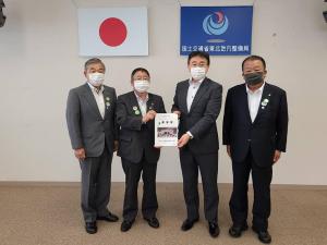 日本国旗と国土交通省 東北地方整備局の旗が壁に掲げられた会場で、スーツ姿の男性4名が並び、市長と男性1名が中心で一緒に要望書を持って記念撮影をしている写真